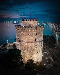 an old tower is lit up at night by the water