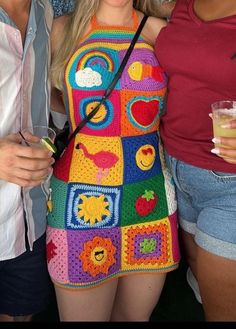 two women standing next to each other with crocheted clothing on and one holding a drink