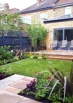 a garden with grass and flowers next to a patio in front of a brick building