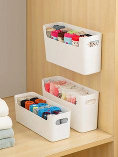 two white bins with different items in them sitting on a wooden shelf next to towels