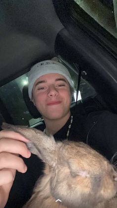 a young man sitting in the passenger seat of a car petting a rabbit with his hand