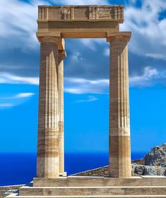 two large pillars with statues on top of them near the ocean and mountains in the background