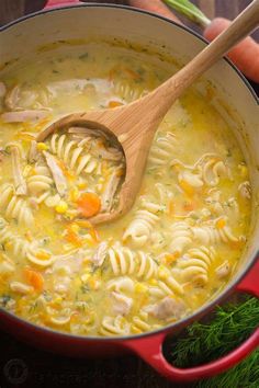 a person holding a wooden spoon in a pot filled with pasta and chicken broth