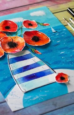 an art project made with paper and watercolors on a wooden table next to a pen