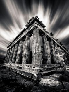 black and white photograph of an ancient temple with clouds in the sky behind it,