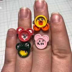 three rings with faces on them are sitting in someone's hand, one is wearing an animal head and the other has a bear