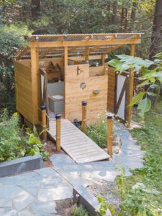 a wooden outhouse in the middle of a wooded area with steps leading up to it