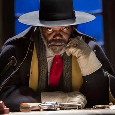 a man in a hat and coat sitting at a table