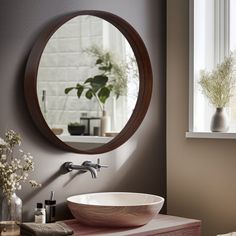 a bathroom sink sitting under a round mirror next to a vase with flowers in it