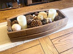 a wooden tray filled with candles and pine cones on top of a rug covered floor