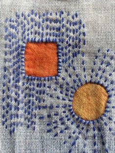 an embroidered piece with blue and orange designs on it's back side, next to a wooden button