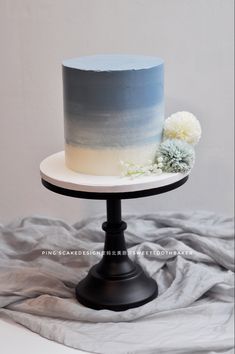 a white and blue ombreed cake on a black stand with flowers in the middle