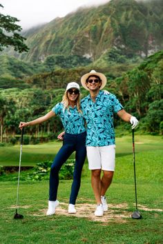 two people standing next to each other on top of a lush green field with mountains in the background