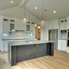 a large kitchen with an island in the middle and two pendant lights hanging from the ceiling