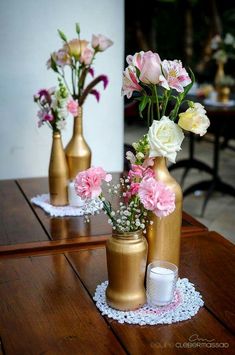 three gold vases with pink and white flowers in them on top of a wooden table