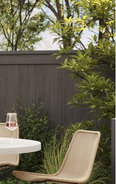 an outdoor table with two chairs and a wine glass sitting on it in front of a fence