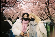 two women standing next to each other in front of trees with pink flowers on them