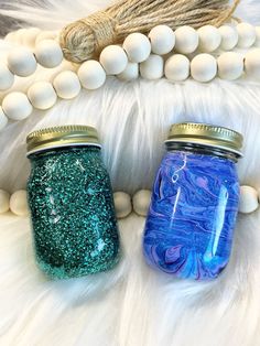 two blue and green mason jars sitting on top of a white fur covered floor next to beads