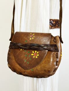 |d e s c r i p t i o n| *circa 1970s *beautiful hippie leather purse from the 70s, came from original owner  *hand tooled design with painted yellow daisies  *saddle flap in front with strap  *a good length arm strap, could be snug cross body purse  *clean inside, well taken care of!  *authentic boho/hippie shoulder bag  |i n f o| tag: none  condition: very good! A few stretches on outside of leather.  |m e a s u r e m e n t s| total length with strap: 22" length of purse: 8.5" height of purse: Vintage Hand-tooled Festival Shoulder Bag, Vintage Brown Bohemian Leather Bag, Hippie Brown Leather Bag, Hippie Leather Shoulder Bag For Everyday, Brown Leather Hippie Bag, Vintage Satchel Shoulder Bag For Festival, Purse Cleaning, Painted Daisy, Daisy Painting