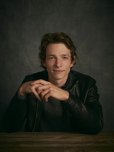 a young man sitting at a table with his hands on his chest and looking to the side