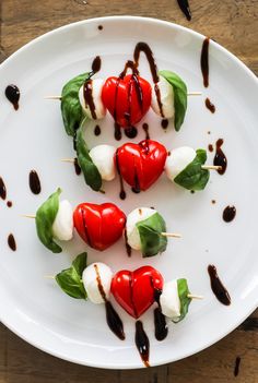 small skewered vegetables are arranged on a white plate with chocolate sauce drizzled over them