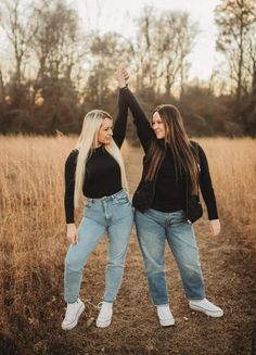 two women in black shirts and jeans are posing for the camera with their arms up