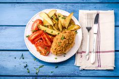 a white plate topped with chicken, potatoes and tomatoes next to a knife and fork