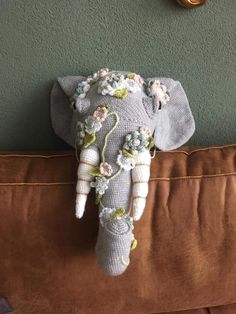 an elephant head with flowers on it sitting on a brown couch next to a clock