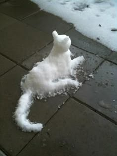 a white stuffed animal laying on top of snow covered ground next to a sidewalk and street