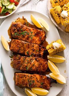 grilled chicken with lemon wedges and corn on the cob next to salad