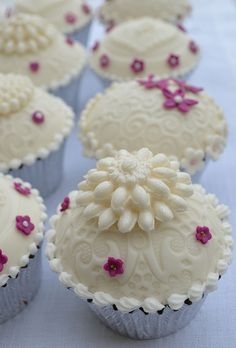 several cupcakes with white frosting and pink flowers on them sitting on a table