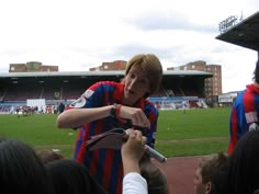 a young man in a striped shirt is holding something up to his face as people watch from the sidelines