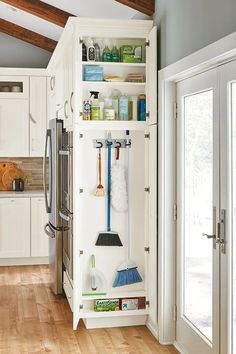 an organized kitchen with white cabinets and wood flooring, including brooms and cleaning supplies