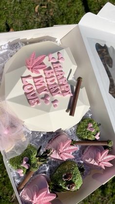 a birthday cake with pink frosting and leaves on it sitting in a white box