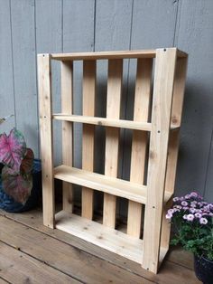 a wooden book shelf sitting on top of a wooden floor next to potted plants