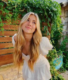 a woman standing in front of a wooden fence wearing a white top and jeans with her hands on her hips