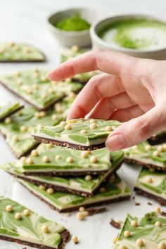 a person reaching for some green food on a table with other foods in the background