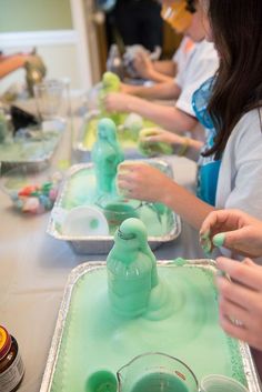 several people are making green slime with plastic cups and spoons on the table