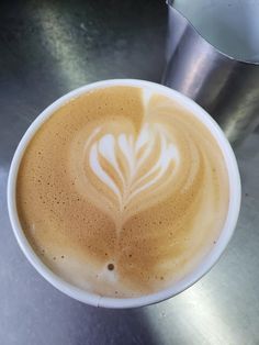 a cappuccino in a white cup on top of a metal countertop