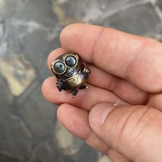 a tiny toy frog sitting on top of someone's hand in front of a stone floor