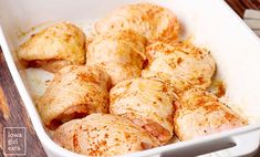 a white casserole dish filled with chicken and seasoning next to a wooden table