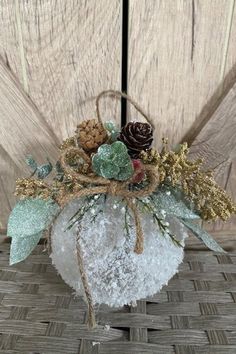 a white heart shaped vase filled with snow and pine cones