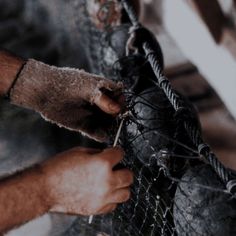 two hands are working on a piece of wire and metal mesh that is being used as a fence