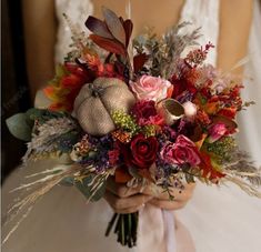 a bride holding a bouquet of flowers in her hands with an orange pumpkin on the side