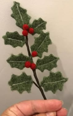 a hand holding a needle felt holly ornament with red berries and green leaves