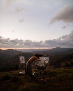 a woman sitting on top of a chair next to an easel in the grass