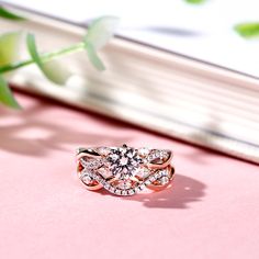 a diamond ring sitting on top of a pink surface next to a book and flower