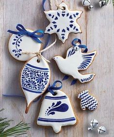 christmas cookies decorated with blue and white designs are on a wooden table next to bells