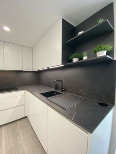 a kitchen with white cabinets and black counter tops is pictured in this image, there are plants on the shelves above the sink