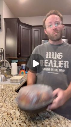 a man holding an object in his hand while standing in front of a kitchen counter